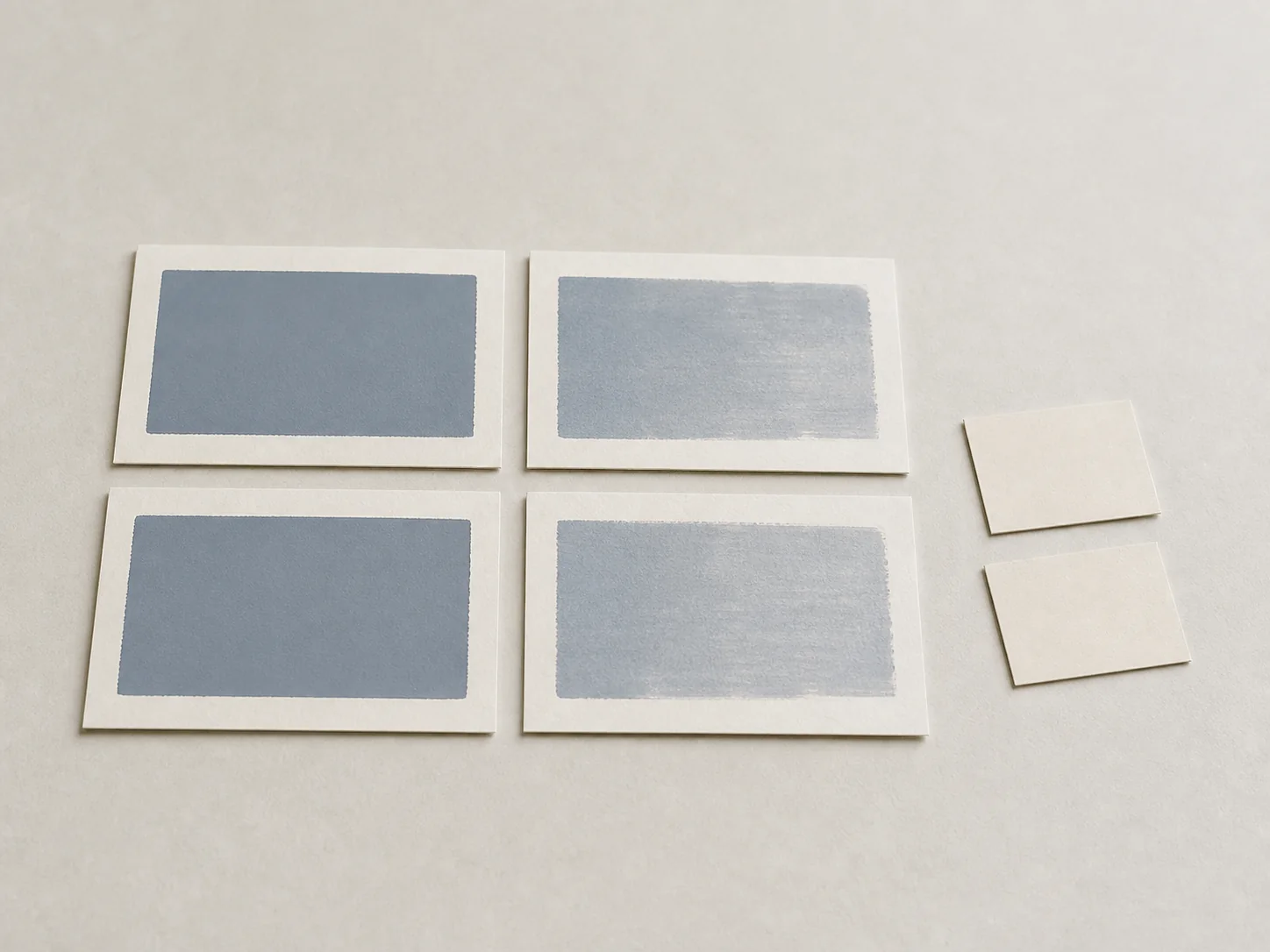 Four anonymous blue-gray print swatches arranged in two comparison pairs beside blank substrate offcuts.